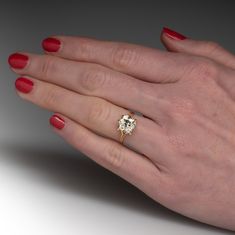 a woman's hand with red nail polish holding an engagement ring