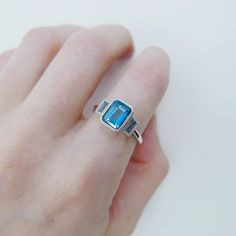 a woman's hand wearing a ring with an aqua blue topazte stone