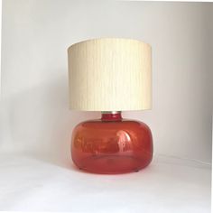 a red table lamp with a white shade on it's base and a beige linen lampshade