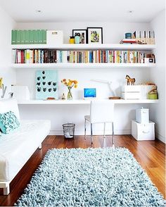 a living room filled with lots of white furniture and bookshelves on the wall