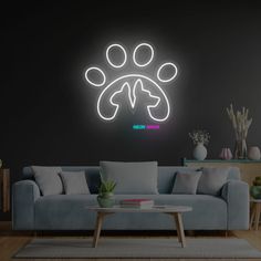 a living room with a couch, coffee table and neon dog paw sign on the wall