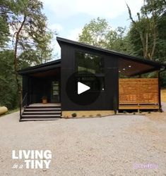 a small black cabin in the middle of a wooded area with stairs leading up to it