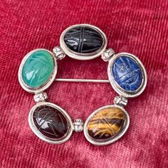 A beautiful vintage Egyptian Revival sterling carved gemstone scarab wreath style brooch by Great Falls Metal Works.  Stones include jade, lapis, tiger's eye & onyx.  Weight is 13 grams and diameter is about 1 3/4".  Excellent vintage condition.  **The box pictured is a photo prop and is not included** Collectible Round Gemstone Brooch, Vintage Gemstone Round Brooches, Ornate Gemstone Brooches For Collectors, Collectible Round Gemstone Brooches, Oval Multi-stone Brooches As Gift, Oval Costume Jewelry Brooch, Vintage Natural Stones Gemstones, Silver Oval Gemstone Brooches, Silver Oval Gemstone Brooch