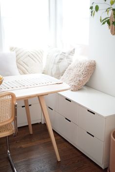 a room with white furniture and pillows on the window sill next to a table