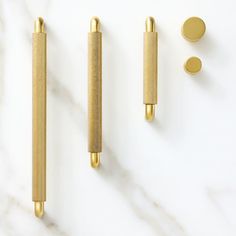 three gold colored objects on a white marble counter top, including two pens and one ballpoint pen