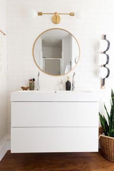 a white bathroom with a round mirror above the sink and plants in front of it