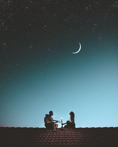 two people sitting on top of a roof watching the moon and stars in the sky