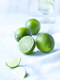 limes with slices cut in half on a white cloth next to a glass of water