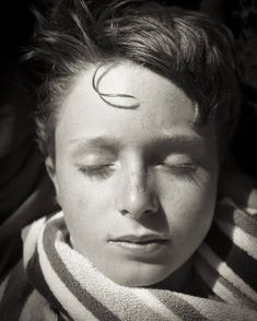 a young boy with his eyes closed wearing a striped shirt and hair in the wind