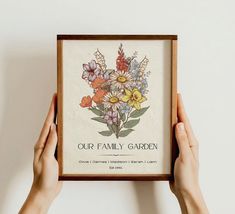 two hands holding up a framed floral print with the words our family garden on it