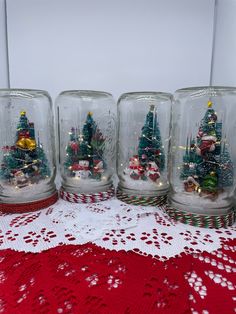 four glass jars with christmas trees in them on a red doily covered tablecloth