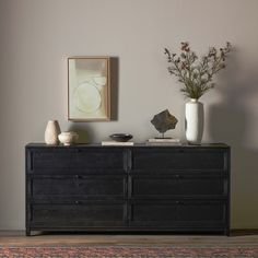 a black dresser with two vases on top of it next to a framed painting