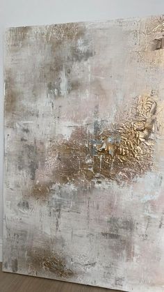 an abstract painting with gold and silver paint on the wall next to a wooden floor