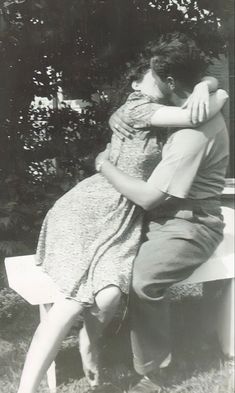 an old black and white photo of a man hugging a woman on a park bench