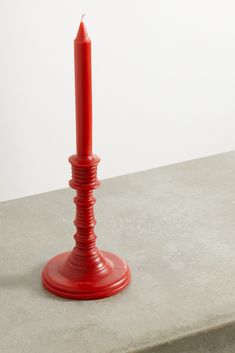 a red candle sitting on top of a cement table next to a white wall and floor