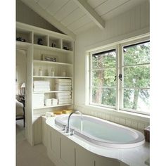 a bath tub sitting next to a window in a room with white walls and floors