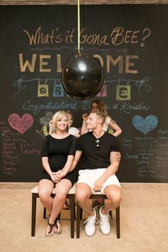 a man and woman sitting next to each other in front of a chalkboard sign