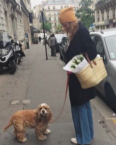 a woman is walking her dog down the street while holding a basket with vegetables on it