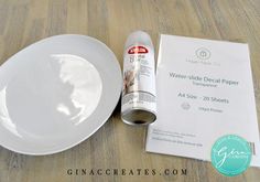 an empty white plate next to a roll of paper on a wooden table with water - side decal papers