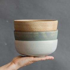 a hand holding three bowls in different colors and sizes, one is white, the other is blue