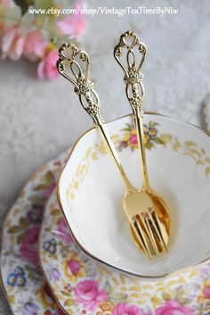 two golden forks sitting on top of a white and pink plate with flowers in the background