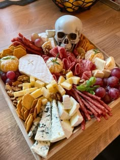 a wooden platter filled with cheeses, meats and other foods next to a human skull