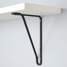 a white shelf with a black handle hanging from it's side on the wall