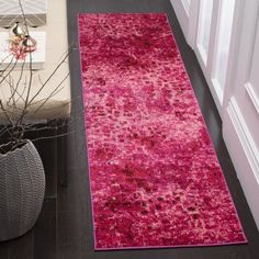 a pink area rug on the floor next to a vase with flowers and a plant