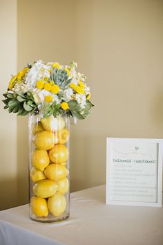 a vase filled with lemons and flowers on top of a table next to a sign