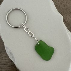 a green sea glass heart keychain sitting on top of a white piece of paper