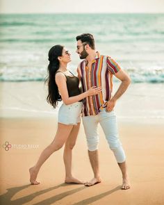 a man and woman standing on top of a sandy beach next to the ocean with their arms around each other