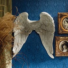 an angel wing hanging on the wall next to two framed pictures and a vase with flowers