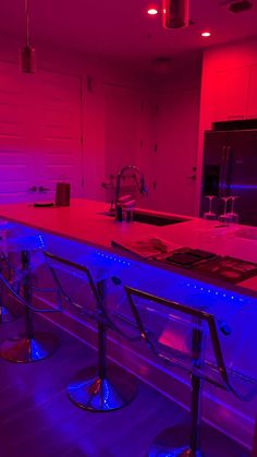 a kitchen with purple lighting and stainless steel barstools on the counter top in front of an oven