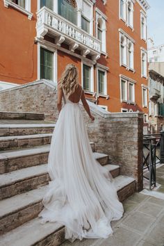 a woman in a wedding dress walking up some steps outside an orange building with white balconies