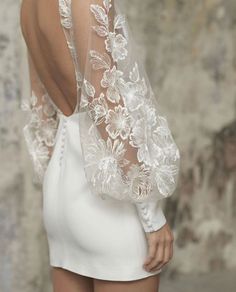 the back of a woman wearing a white dress with sheer sleeves and flowers on it