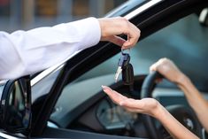 two people handing keys to each other out of a car window with the driver's hand on the steering wheel