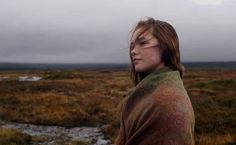 a woman standing in the middle of a field with a bird on her shoulder and head