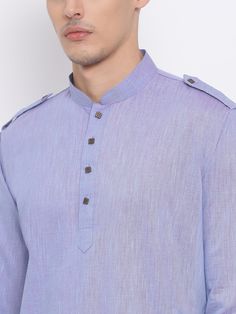 a man wearing a blue shirt with buttons on the chest and collar, standing against a white wall