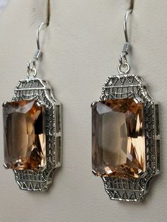 Simulated Peach Topaz EarringsLantern Design#E13 Inspired by the Art Deco period, these lovely antique reproduction earrings are sterling silver. Created from an antique brooch, each earring has a 9 carat simulated Peach Topaz surrounded by sterling silver filigree. The man-made gemstones are 15mm x 12mm each. The earrings are 1 3/4" long and 9/16" at their widest point. These lovely dangle earrings are marked 925 for sterling silver. These earrings are a wonderful blend of today and yesteryear. Silver Rectangular Stone Earrings For Formal Occasions, Elegant Rectangular Filigree Jewelry, Elegant Silver Rectangular Earrings, Elegant Nickel-free Rectangular Jewelry, Sterling Silver Rectangular Earrings For Wedding, Elegant Rectangular Jewelry With Intricate Design, Sterling Silver Wedding Earrings With Rectangular Shape, Vintage Rectangular Formal Earrings, Antique Jewelry With Rectangular Stone For Formal Occasions