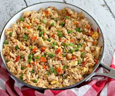 a pan filled with rice and vegetables on top of a red and white checkered cloth