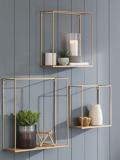 two gold metal wall shelves with plants and candles on them, against a blue painted wall