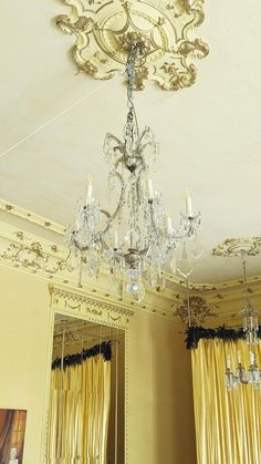 a chandelier hanging from the ceiling in a room with yellow drapes and curtains