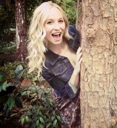 a woman is smiling as she hides behind a tree