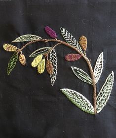 a close up of a piece of embroidery on a black cloth with green, yellow and red leaves