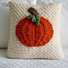 a crocheted pumpkin pillow on a white couch with an orange and green applique