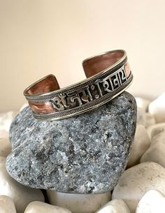 "This beautiful Om Namah Shivaya cuff bracelet is made in Nepal. Size: 18cm - As It's open-ended, would fit most hands Width - 15mm approx Weight - 23gms approx Material: white metal, brass, copper To fit the bracelet open it up so the gap is wide enough to pass over the narrowest part of your wrist and then squeeze it back into shape until it is a nice comfortable fit. Om Namah Shivaya (Devanagari: ॐ नमः शिवाय;[1] IAST: Om Namaḥ Śivāya) is one of the most popular Hindu mantras and the most impo Bohemian Adjustable Engraved Bangle, Handmade Adjustable Spiritual Bangle, Handmade Symbolic Cuff Bracelet For Festivals, Engraved Bangle Bracelets For Festival, Handmade Spiritual Bangle For Festivals, Handmade Silver Spiritual Wristband, Handmade Spiritual Silver Wristband, Adjustable Symbolic Bangle Bracelet, Adjustable Round Spiritual Cuff Bracelet