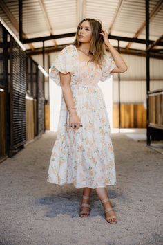 The Peachy Dress is a summer must-have for any fashion-forward woman. The cream and peach floral print adds a touch of femininity, while the ruffled neckline and short bubble sleeves provide a playful touch. The smocked bodice with contrast thread not only adds dimension, but also ensures a perfect fit. With tiered ruffle trim, pockets, and a lined midi length, you'll stay comfortable and stylish all season long. Haylee is wearing size small