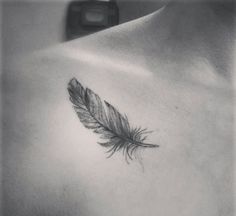 a black and white photo of a woman's chest with a feather tattoo on it