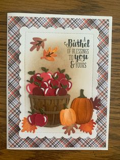 a handmade card with apples and pumpkins in a basket on a wooden table