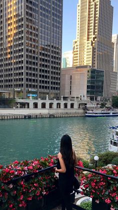 a woman is standing on a balcony overlooking the water and flowers in front of her